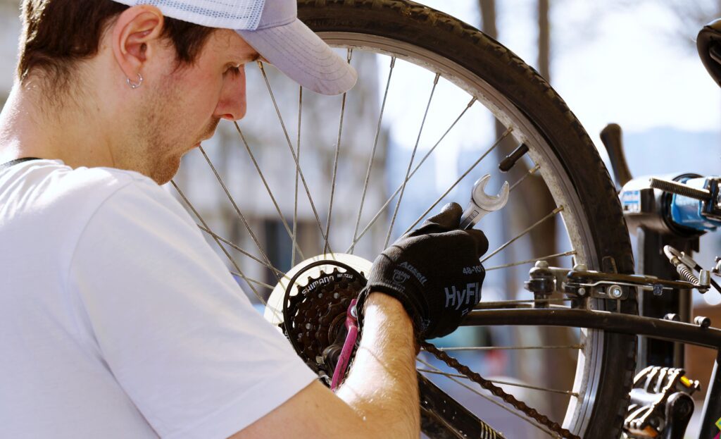 Photo d'un mécanicien resserrant la roue arrière d'un vélo en extérieur dans le cadre d'une formation mécanique vélo en entreprise.