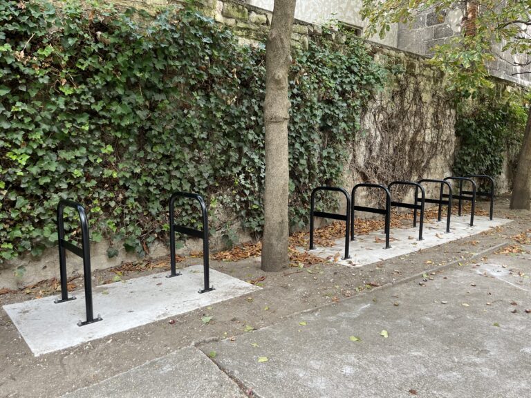 Photo de 8 arceaux de stationnement vélo disposés de part et d'autre d'un arbre dans une cour d'immeuble.