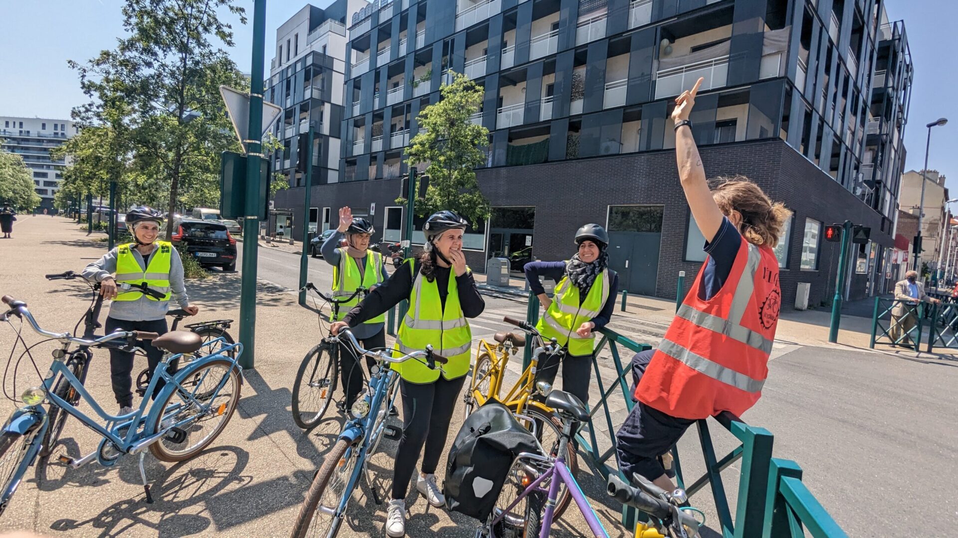 Photo d'un groupe de cyclistes élèves de la vélo-école écoutant les explications de l'éducatrice à l'angle d'une rue.