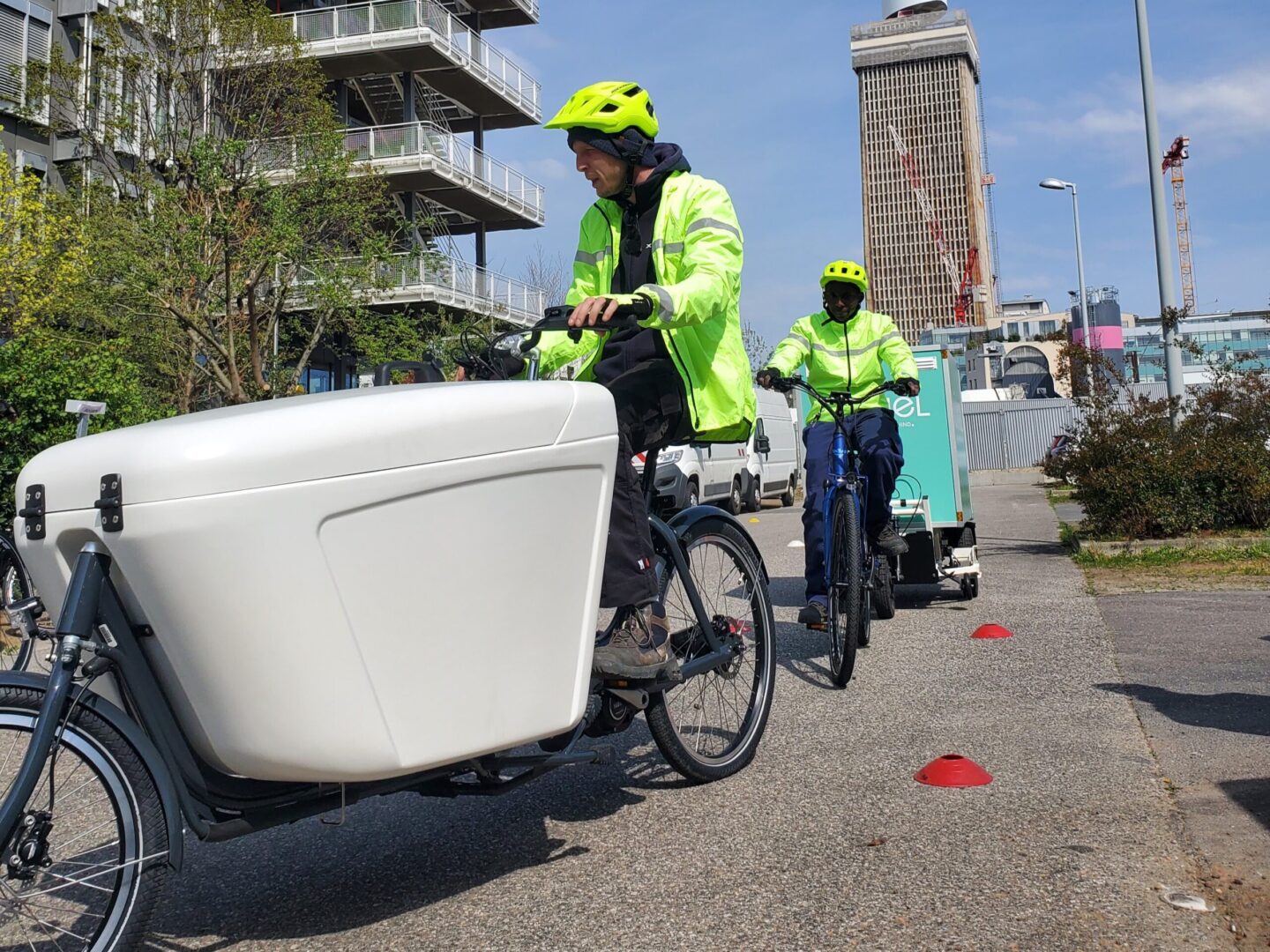 Photo de deux cyclistes conduisant respectivement un biporteur et un vélo électrique avec remorque assistée.