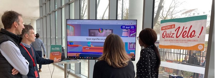 Photo d'un groupe de participants devant une animation de quiz vélo dans le hall d'une entreprise.