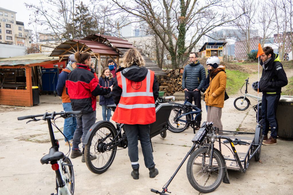 Photo d'un groupe de participants et participantes à une formation cyclologistique, avec plusieurs types de vélos cargos.