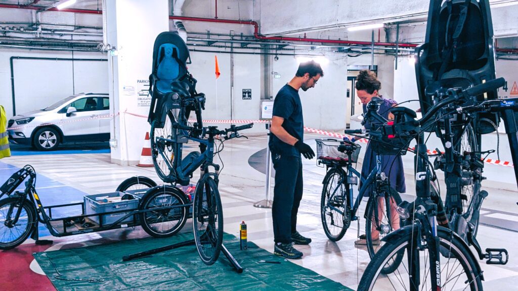 Photo d'un mécanicien accueillant une cliente avec son vélo lors d'un atelier de réparation mobile dans le sous-sol d'une entreprise.