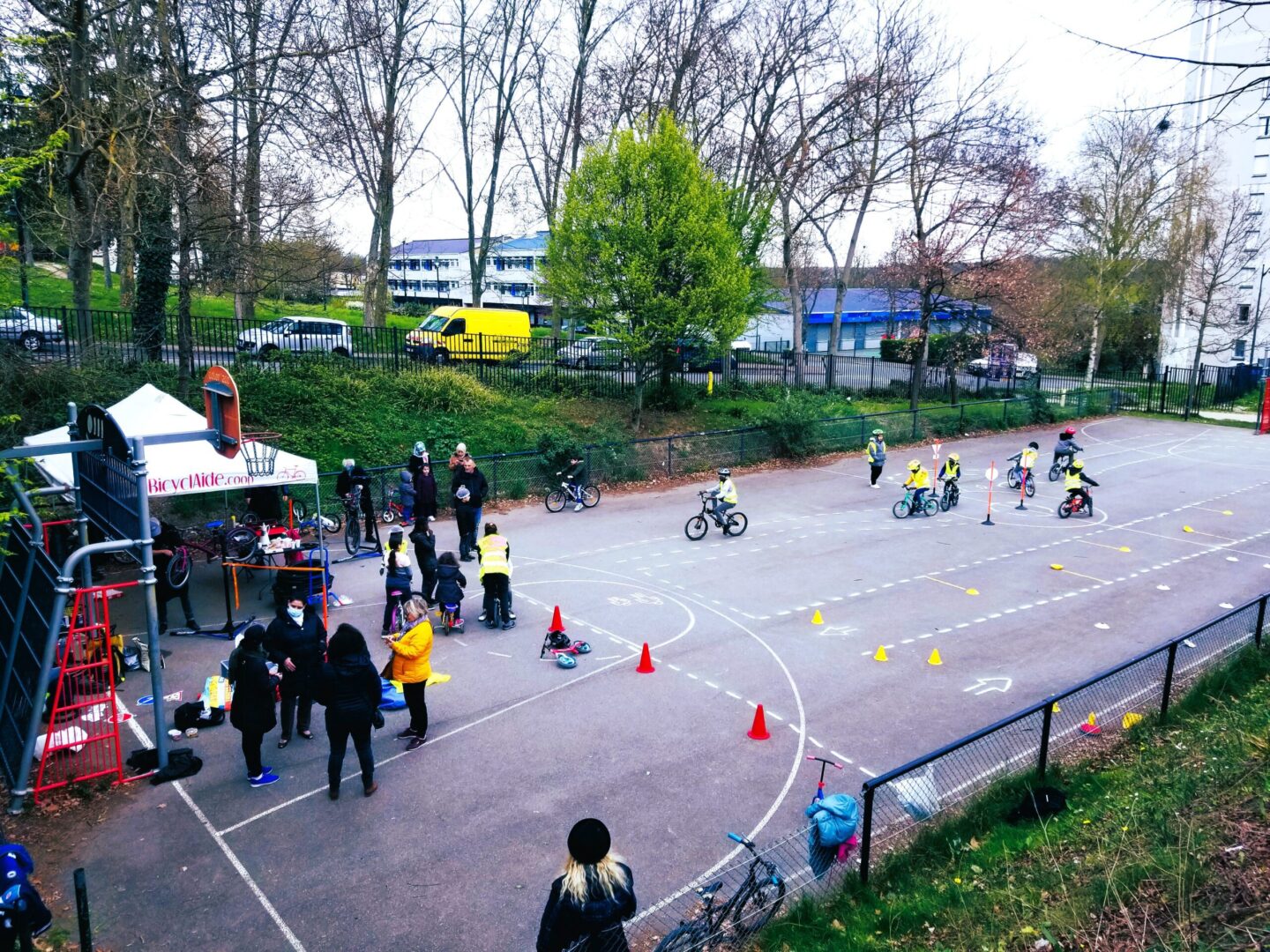 Photo surplombante d'une esplanade où sont organisés un atelier de réparation de vélo mobile et un parcours ludique, avec de nombreux enfants et adultes.