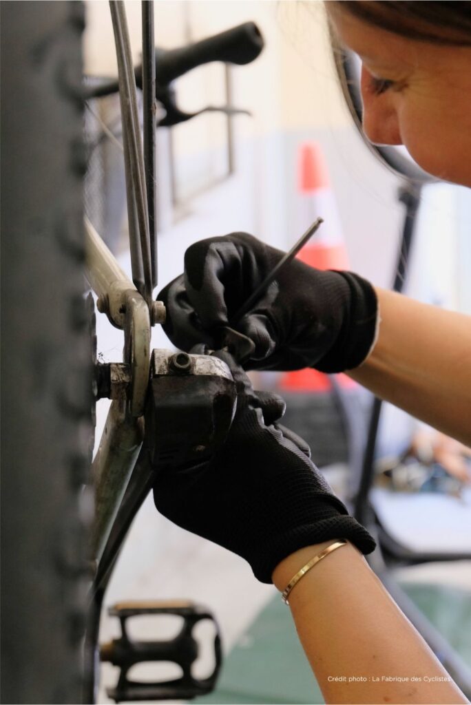 Photo d'une mécanicienne travaillant sur le dérailleur d'un vélo lors d'un atelier mobile.