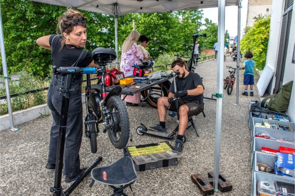 Photo d'une mécanicienne réglant les freins d'un vélo lors d'un atelier mobile sous un barnum.