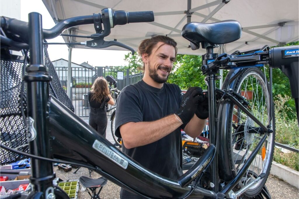 Photo d'un mécanicien resserrant les cables de frein d'un vélo lors d'un atelier mobile.