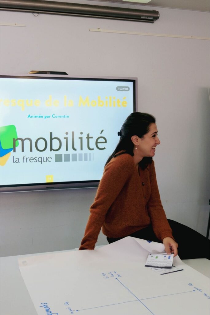 Animatrice de la Fresque de la mobilité devant une télévision qui projette le logo de la Fresque