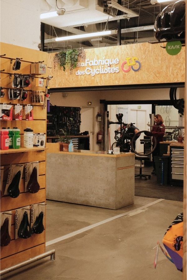 Photo de l'intérieur de l'Atelier boutique avec un comptoir, un présentoir pour accessoires, et des vélos en fond
